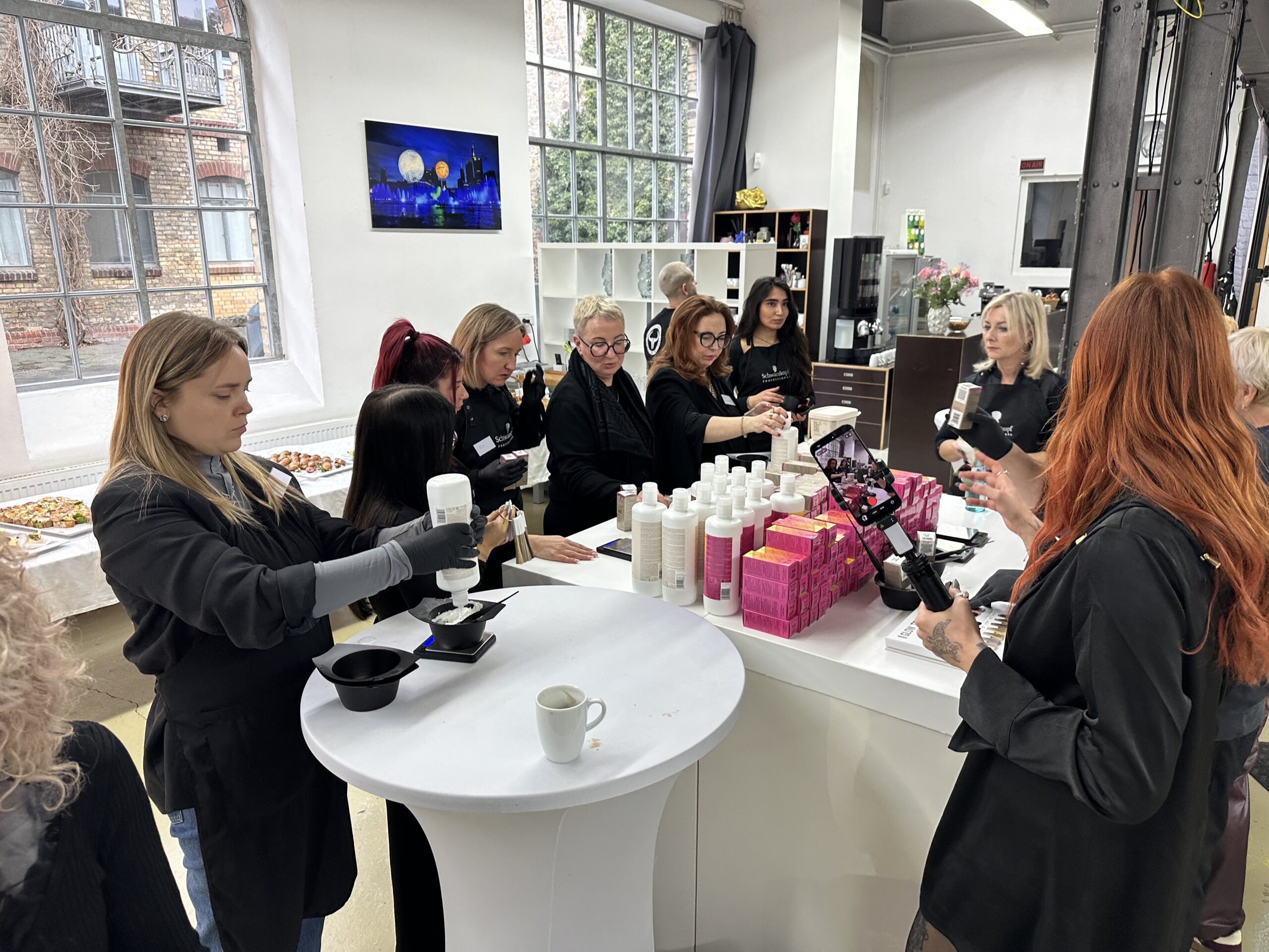 Teilnehmerinnen eines Friseur-Seminars mischen Produkte an Stationen im WackerLoft unter Aufzeichnung mit einem Smartphone.