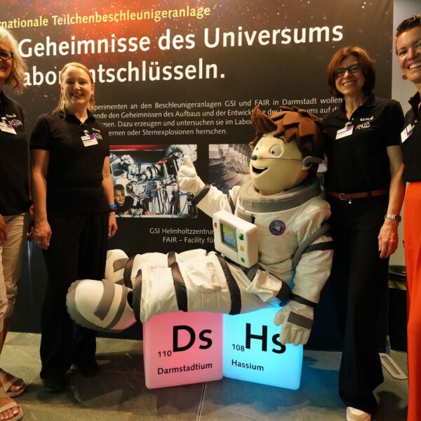 Das Team von GSI und FAIR am Expolink Messestand in Berlin zusammen mit einem Maskottchen auf leuchtenden Element-Würfeln.